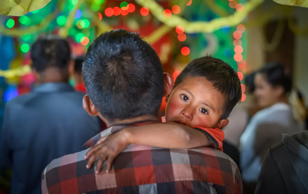 Adult embracing a child, with colorful decorations in the background