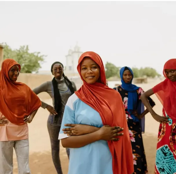 Women in reddish orange headscarves standing side by side outdoors