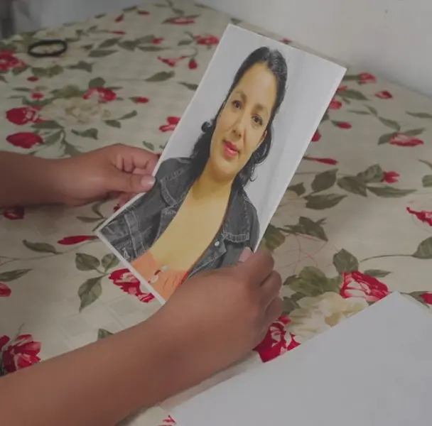 Hands holding a printed photo of a smiling woman over a flowered cloth