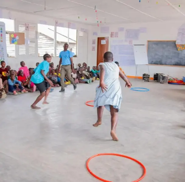 Children gathered in a large hall for a group activity, with hoops on the floor