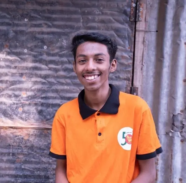 Smiling boy in an orange shirt standing in front of a corrugated metal wall